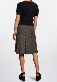 Musta lyhythihainen neule yhdistettynä polvipituiseen moniväriseen kalanruotokuvioiseen hameeseen. Mustat kiilakantaiset sandaalit täydentävät asun.