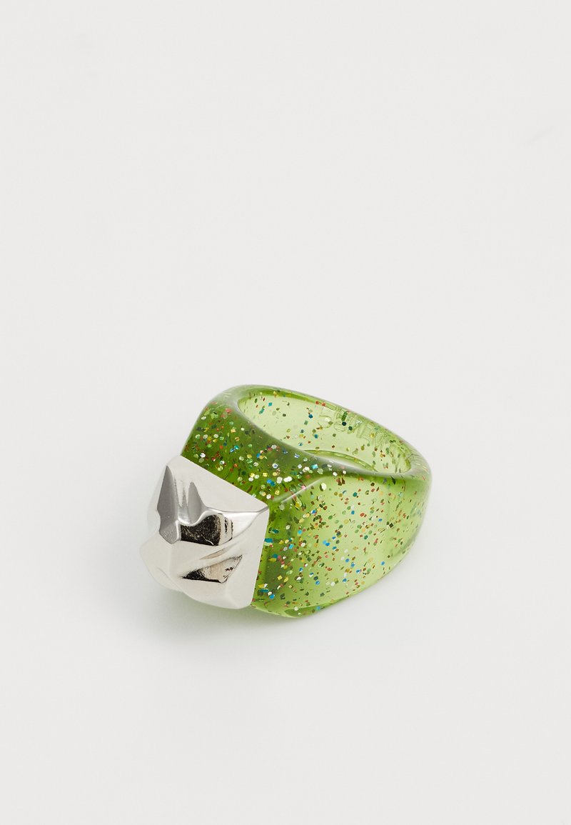 Grön glittrande har ring med en kraftig silverdetalj. Slät yta och rund form. Glittrande partiklar utspridda i materialet.