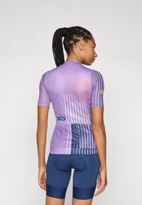Maglia da ciclismo viola a maniche corte con un motivo a righe geometriche arancioni, verdi e blu navy. Abbinata a pantaloni ciclistici blu navy.