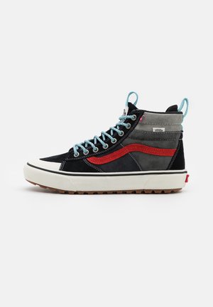 High-Top Vans Sneaker in Schwarz und Grau mit rotem Streifen, blauen Schnürsenkeln, weißer Sohle und braunem Profil, von der Seite auf weißem Hintergrund gezeigt.