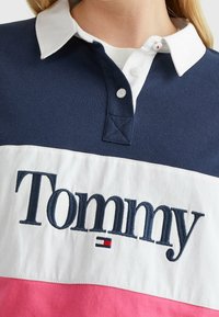 Marineblaues und weißes Poloshirt mit gesticktem "Tommy"-Logo, versehen mit einem weißen Kragen und einem rosa Streifen am Saum. Knöpfe am Kragen.