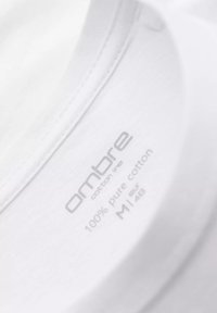 Hvid bomulds T-shirt mærke, der viser "ombre cotton line," mærket 100% ren bomuld, størrelse M, med minimalistisk grå tekst på en ensfarvet baggrund.