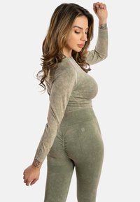 Maglietta athletic a maniche lunghe di colore verde oliva con tessuto texturizzato e polsini a costine, abbinata a leggings a vita alta coordinati con dettagli arricciati.