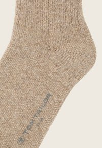 Beige ribbet sok lavet af tekstureret stof. Har en forstærket hæl og tå, med "TOM TAILOR" logo trykt i blåt nær anklen.