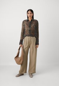 Kergel läbipaistev pruun blousee, millel on värviline paisley print, nööbiga lukustus ja pikad varrukad; beežid laiade jalgade püksid; pronksist käekott; kootud jalanõud.