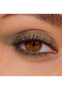 Närbild av ett öga med guld- och olivgrön ögonskugga, långa svarta ögonfransar och bruna iris. Hudens struktur är slät och ljus.