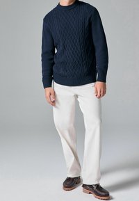 Granatowy sweter z dzianiny o teksturowanym wzorze w warkocze, zestawiony z białymi spodniami i ciemnymi butami z gumową podeszwą oraz brązowymi akcentami.