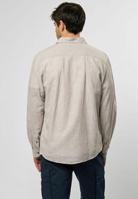 Hellbeige Langarmhemd mit einem subtilen gewellten Muster, Knopfmanschetten und einem abgerundeten Saum, von hinten gezeigt.