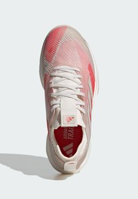 Zapatilla deportiva blanca y rosa con una parte superior texturizada y transpirable, refuerzo en el talón y detalles del logo en la lengüeta y el lateral.