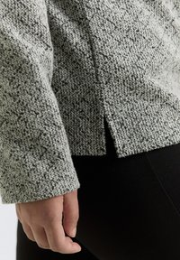 Textured grey sweater with a soft, woven pattern, featuring a side slit and long sleeves. The fabric appears warm and thick.