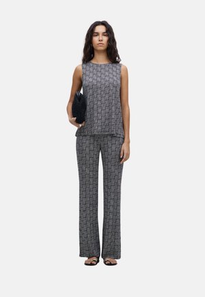 Conjunto de dos piezas que incluye una blusa sin mangas de estampado y pantalones de pierna ancha a juego en blanco y negro. Tejido texturizado, acompañado de un bolso de mano negro de punto.
