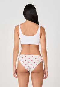 Bralette de algodón blanco con tirantes anchos, combinado con braguitas blancas de canalé que presentan un pequeño estampado de fresas rojas en toda la prenda.
