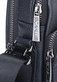 Borsa nera in pelle con materiale texture, ferramenta in argento, dettaglio con zip e una tracolla spessa con una fibbia distintiva.