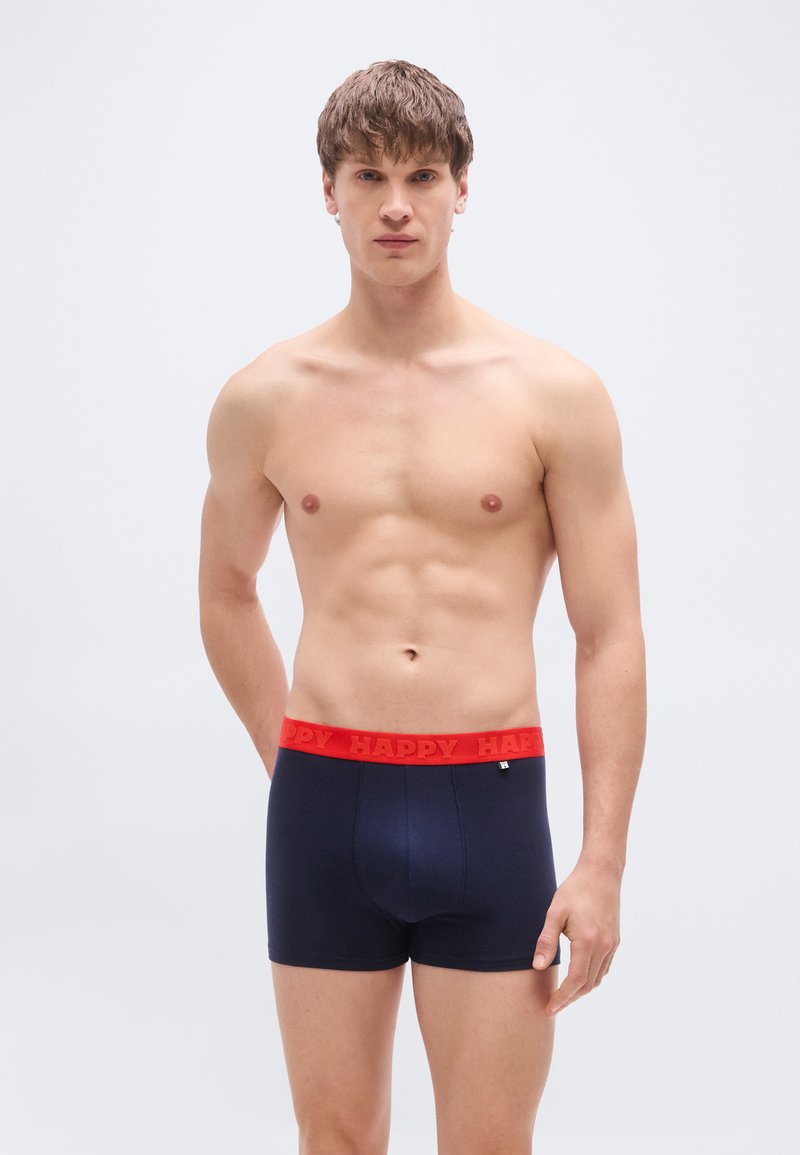 Σκούρα μπλε ανδρικά εσώρουχα σορτς με κόκκινη ελαστική μέση που φέρει τη λέξη "HAPPY" με έντονα γράμματα, κατασκευασμένα από μαλακό, ελαστικό υλικό.