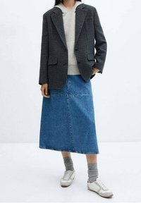 Blazer in grijs houndstooth patroon, gecombineerd met een lichtgrijze hoodie, een blauwe denim maxi rok, grijze sokken en witte sneakers.