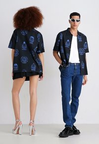 Zwart T-shirt met korte mouwen en een blauw grafisch ontwerp, gecombineerd met hoge denim jeans en zilveren hoge hakken.