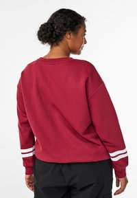 Bordeaux sweatshirt med en afslappet pasform, ribbet halsudskæring og hvide striber ved ærmerne. Blød tekstur; har en lige kant.