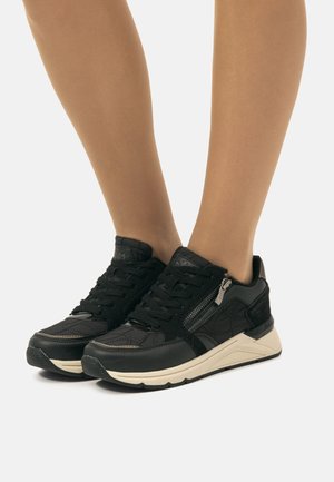 Zapatillas negras con acabado texturizado, con un detalle de cremallera, parte frontal con cordones y una suela blanca contrastante. Diseño liso y acolchado.
