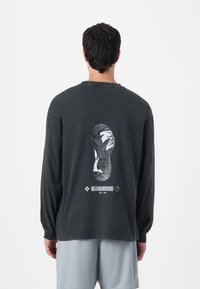 Black long-sleeve shirt with a graphic of a shoe sole on the back. Casual design, relaxed fit, textured cotton material.