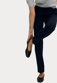Marine blauwe tailored broek met een rechte snit, voorzien van een trekkoord in de taille en omgeslagen zoom, gecombineerd met zwarte platte schoenen.