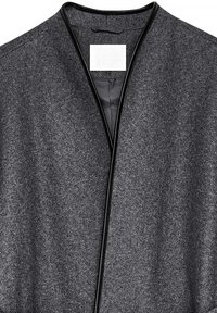 Grå uldwrap med mat finish, prydet med sort læderkant omkring halsen, og et mærke i midten. Minimalistisk design.