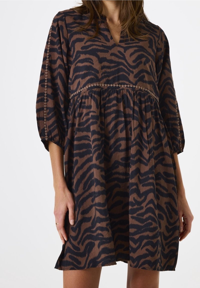 Femme portant une robe imprimé zèbre marron et noir avec des manches trois-quarts et des détails de broderie sur les manches et la taille.