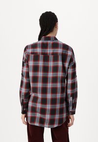 Camicia a quadri nera con motivi a reticolo rossi e blu, maniche lunghe e orlo curvo. Il materiale sembra leggero con una trama liscia.