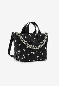 Sac tissé noir avec des pois blancs, poignées robustes et accent en chaîne argentée. Présente une forme structurée et une texture lisse.
