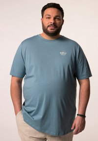 Camiseta de manga corta azul claro con cuello redondo y un sutil gráfico blanco en el pecho. Tela suave, corte holgado y dobladillo curvado.