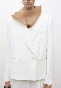 Bílý dvouřadý blazer s volným střihem, textured látkou a dvěma knoflíky. Nosený s béžovým šátkem kolem krku.
