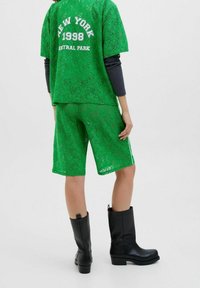 Zielony koronkowy strój składający się z luźnej koszulki z napisem „NEW YORK 1998 CENTRAL PARK”, do której dopasowano krótkie spodenki i czarne kozaki za kolano.