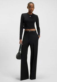 Top nero a maniche lunghe cropped con logo, abbinato a pantaloni a gamba larga con vita alta. Gli accessori includono una piccola borsa nera e una cintura.