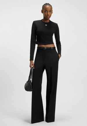 Top negro de manga larga recortado con logo, combinado con pantalones de pierna ancha de cintura alta. Los accesorios incluyen un pequeño bolso negro y un cinturón.