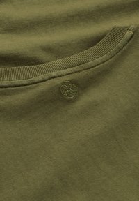 Nahaufnahme eines olivgrünen Stoffs mit geripptem Kragen und einem dezenten, stickierten runden Muster nahe der Naht.