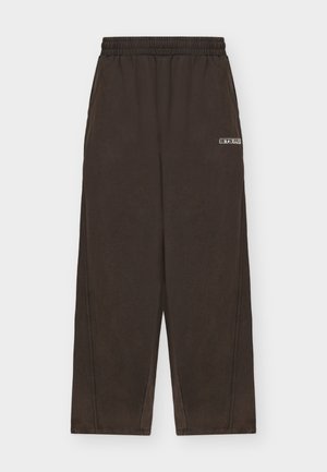 Hnědé volné kalhoty s elastickým pasem. Mají boční kapsy a malé logo. Materiál má hladkou texturu s minimálním leskem.