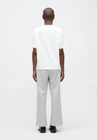 Λευκό κοντομάνικο μπλουζάκι συνδυασμένο με ανοιχτό γκρι φόρμες, με χαλαρή εφαρμογή και διακριτή υφή. Μαύρα παπούτσια ολοκληρώνουν το σύνολο.