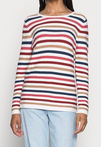 Pull à manches longues rayé en blanc, rouge, bleu, marron et rose. Doté d'un col rond et d'un tissu texturé. Associé à un jean bleu clair.