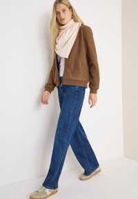 Veste en polaire texturée marron, écharpe rose clair, jeans à jambes larges bleus et baskets beiges avec des accents blancs et verts.