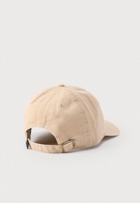 Μπέζ βαμβακερό καπέλο με κυρτή βρύση, ρυθμιζόμενο λουράκι στο πίσω μέρος και κουμπί στην κορυφή. Ομαλή υφή και απλός σχεδιασμός.