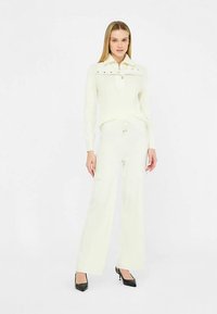 Pull en maille côtelée blanche avec un col et un détail de boutons, associé à un pantalon large assorti, doté d'une ceinture élastique confortable.
