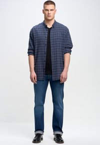 Conjunto masculino que incluye una camisa de cuadros en tonos azul y gris, camiseta negra, jeans azules y zapatos negros con un acabado suave.