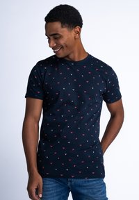Námornícky modré bavlněné tričko s kulatým výstřihem, krátkými rukávy a opakujícím se malým červenobílým geometrickým vzorem po celém povrchu.