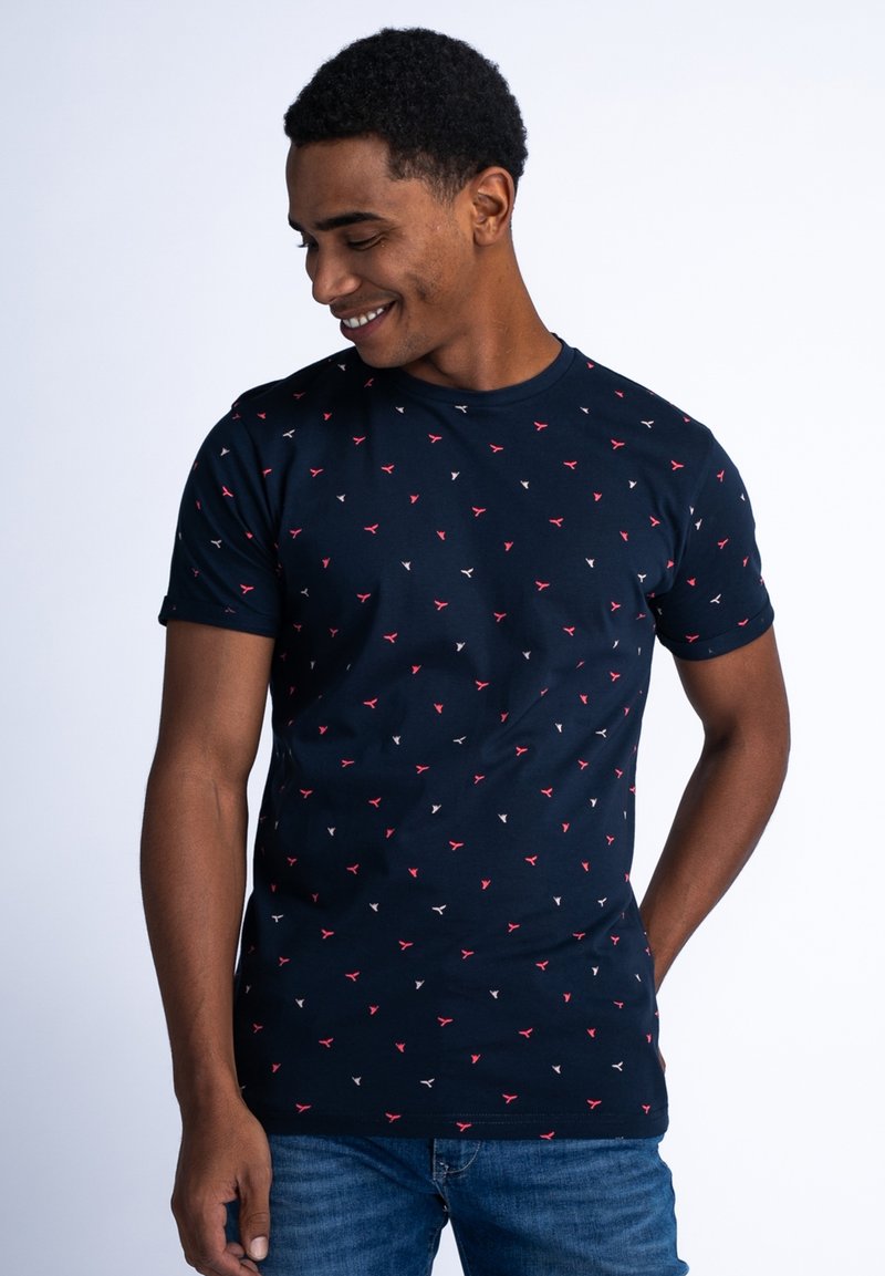 Námornícky modré bavlněné tričko s kulatým výstřihem, krátkými rukávy a opakujícím se malým červenobílým geometrickým vzorem po celém povrchu.