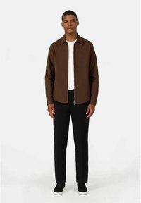 Brun zip-up jakke med ståkrage, båret over en hvit skjorte, kombinert med svarte bukser og svarte joggesko. Enkel, strømlinjeformet design.