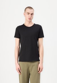 Black cotton T-shirt with a crew neck, short sleeves, and a relaxed fit. Model wears olive green pants. Simple design with no patterns.