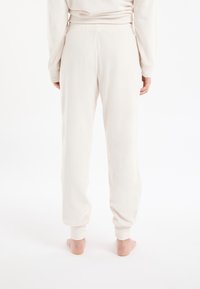 Lichtbeige sweatpants met een geribbelde structuur, voorzien van een elastische tailleband en taps toelopende pijpen, achterkant gezien.