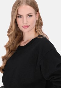 Zwart sweatshirt met een ronde hals en lange mouwen, gemaakt van zacht materiaal. Heeft een subtiele textuur, zonder zichtbare patronen of sieraden.