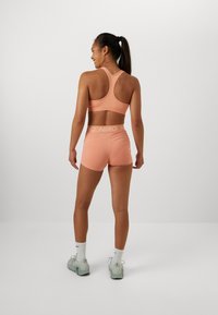 Peach sports bra and shorts set with a racerback design. Shorts feature a NIRO waistband. Model wears white socks and light green sneakers.