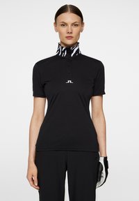 Sort polo skjorte med korte ærmer, der har en høj krave i zebramønster. Inkluderer en tre-knaps stolpe og logo detaljer på forsiden.