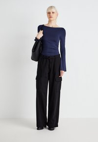 Tengerészkék, hosszú ujjú felső, slim fit fazonnal és hajó nyakkivágással, fekete, bő szárú cargo nadrággal párosítva, oldalsó zsebekkel és övvel a derékrészen. Fekete táska.